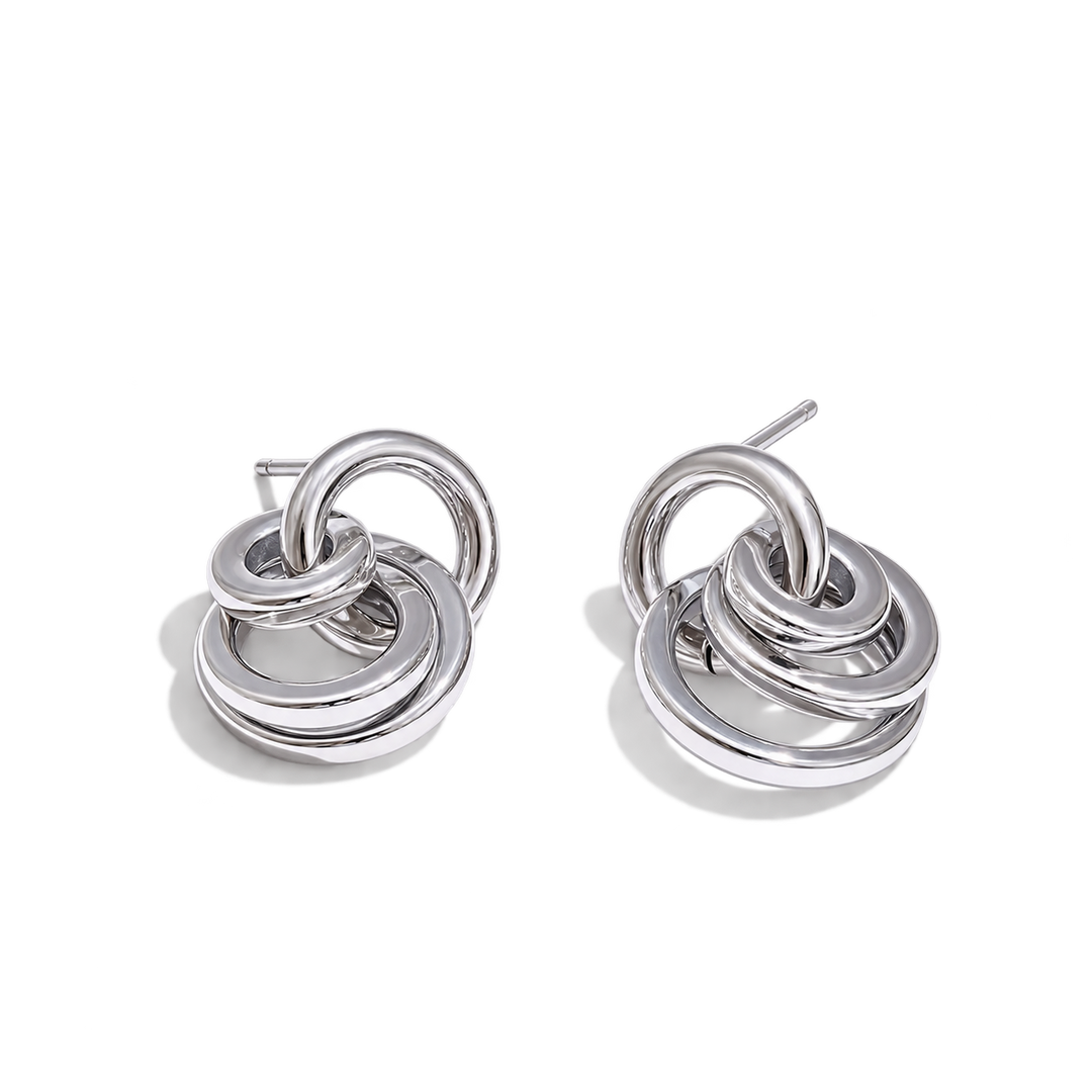A pair of polished silver-toned drop earrings with interlocking concentric rings, shown on a clean white background.