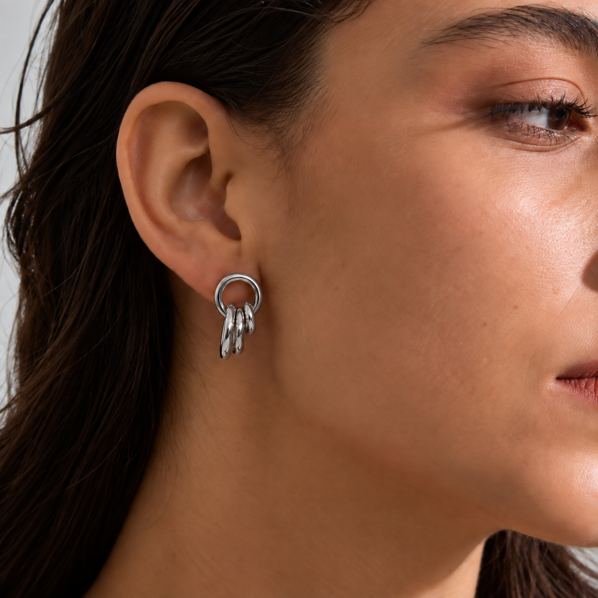 A close-up of a model's ear wearing a silver hoop earring with three dangling textured rings.
