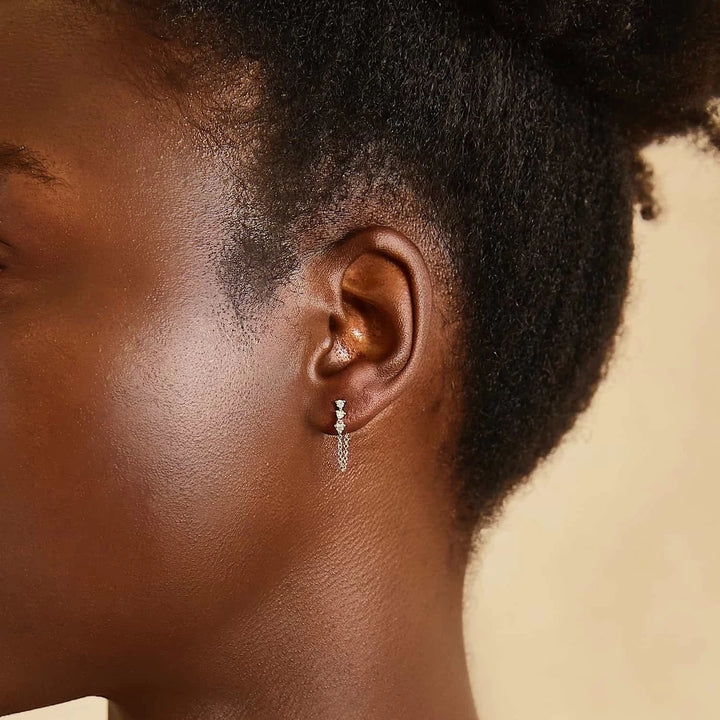 Close-up of an ear wearing a diamond earring with a neutral background