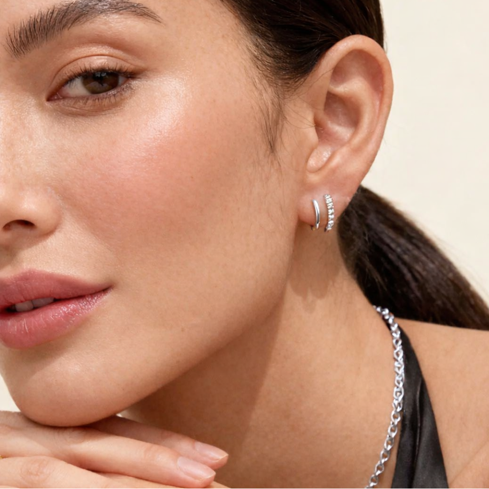 Close-up of a woman wearing silver hoop earrings and a necklace against a neutral background