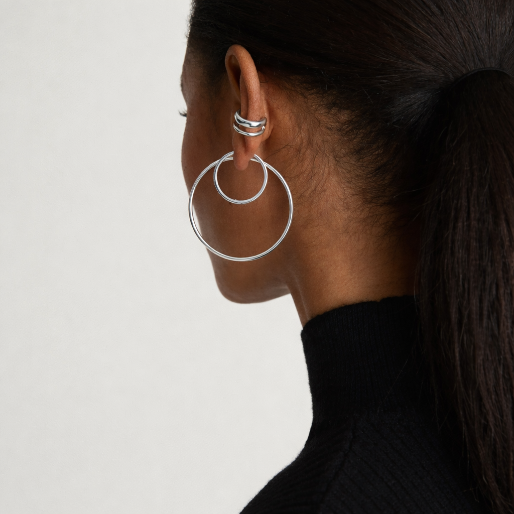 Close-up of a person wearing a silver hoop earring on a plain background