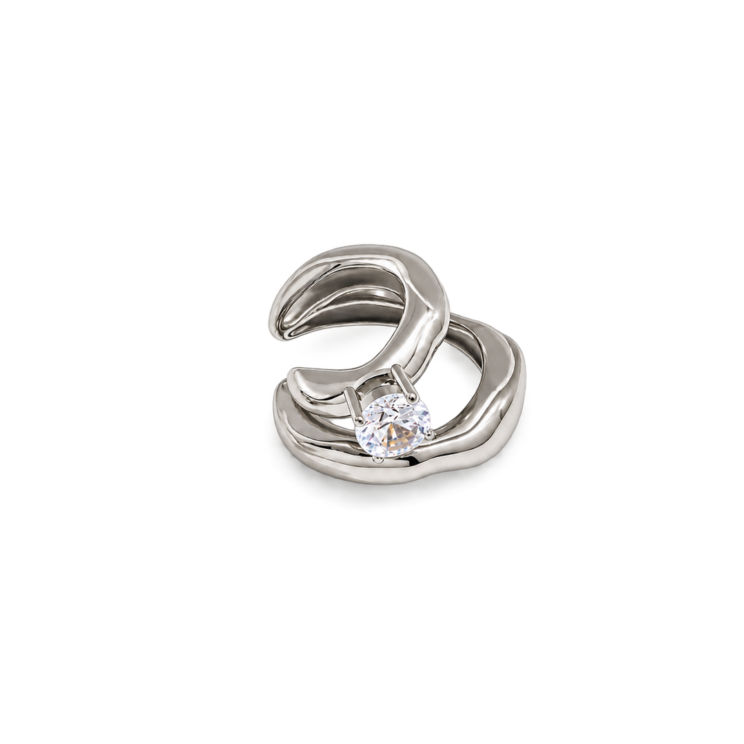 A silver-toned abstract wave-shaped ring with a single round clear gemstone, shown on a plain white background.