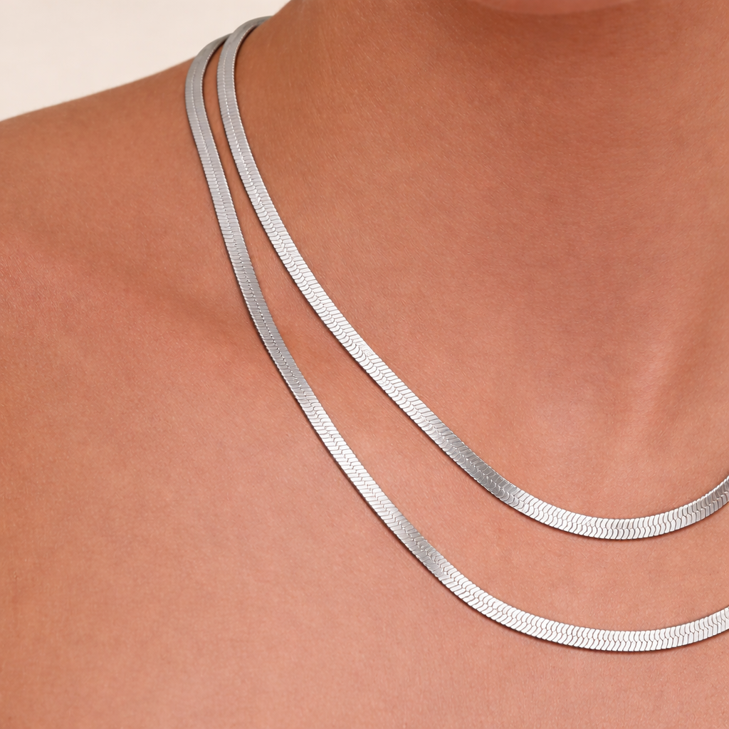 Silver snake chain necklace on a person's neck against a beige background