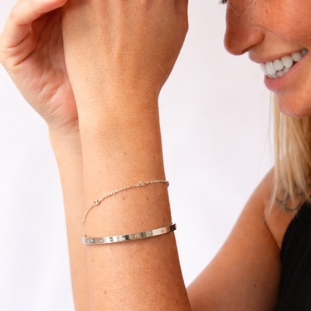 Woman wearing two silver bracelets on a plain background