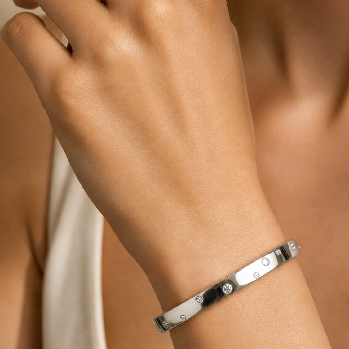Close-up of a hand wearing a silver bracelet on a neutral background