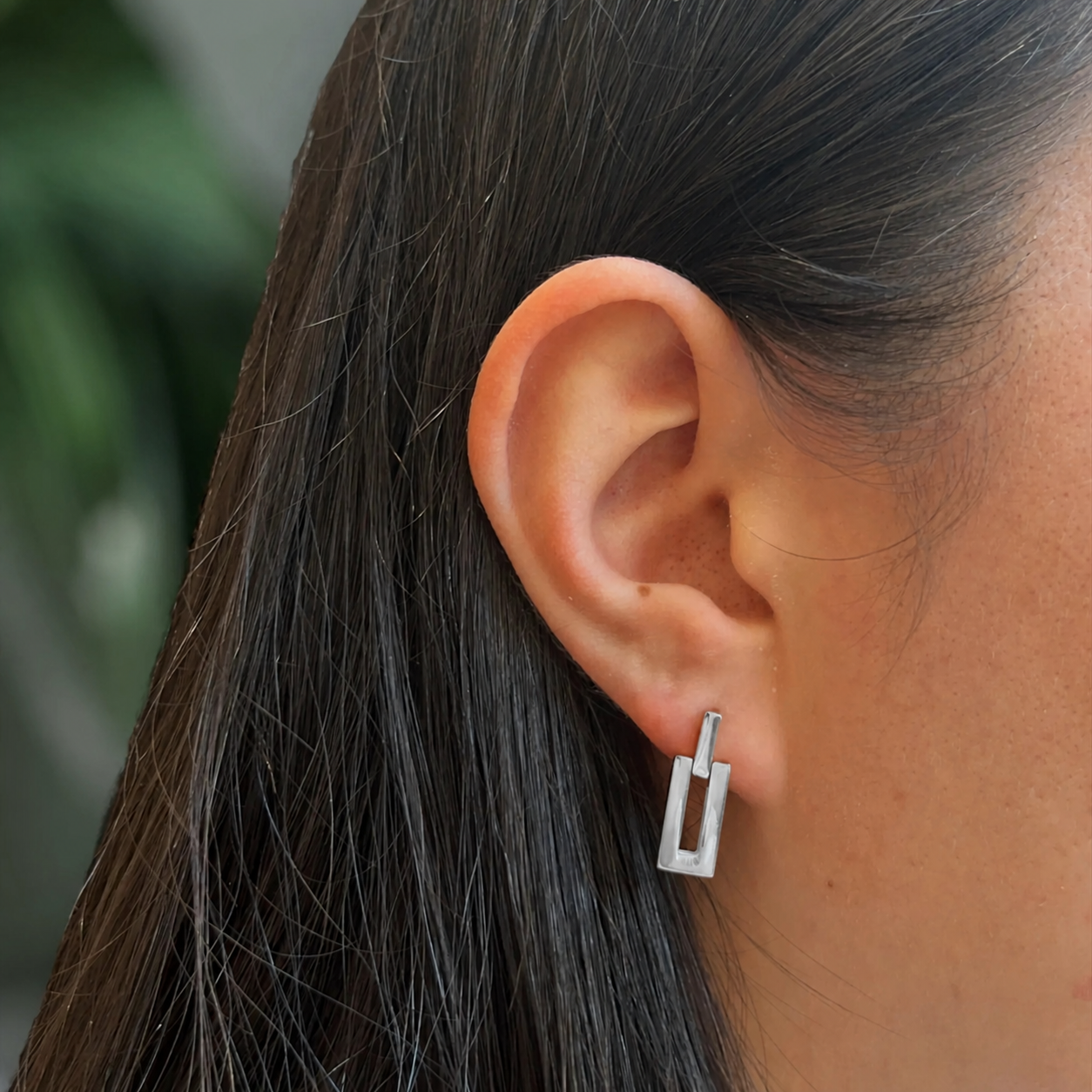 Close-up of an ear wearing a silver earring with dark hair and blurred background