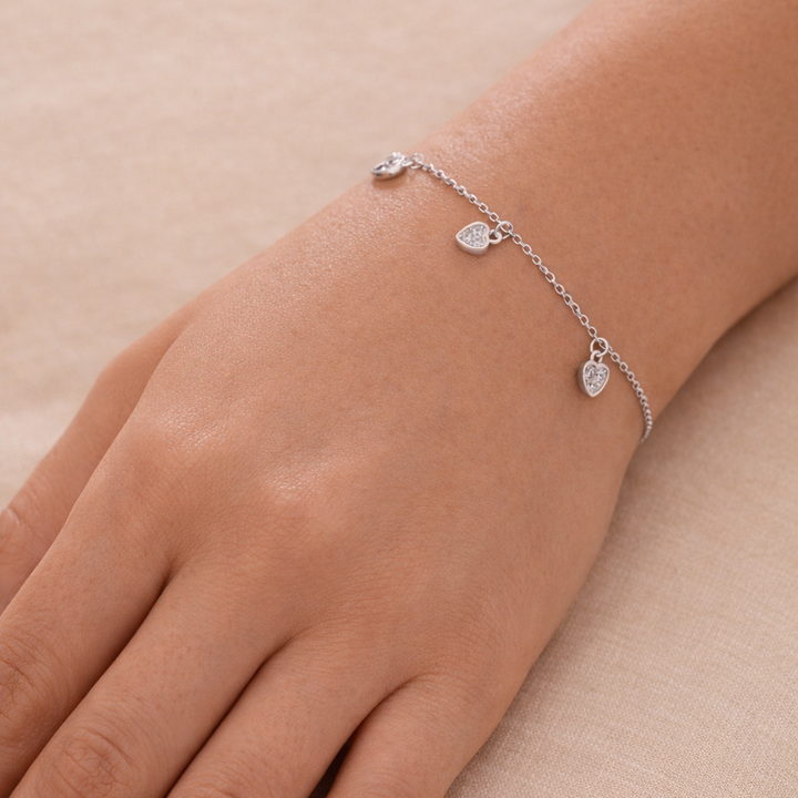 Silver bracelet with heart charms on a wrist against a beige background