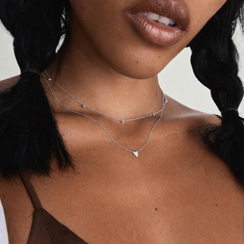 Close-up of a person wearing a delicate silver necklace with a plain background