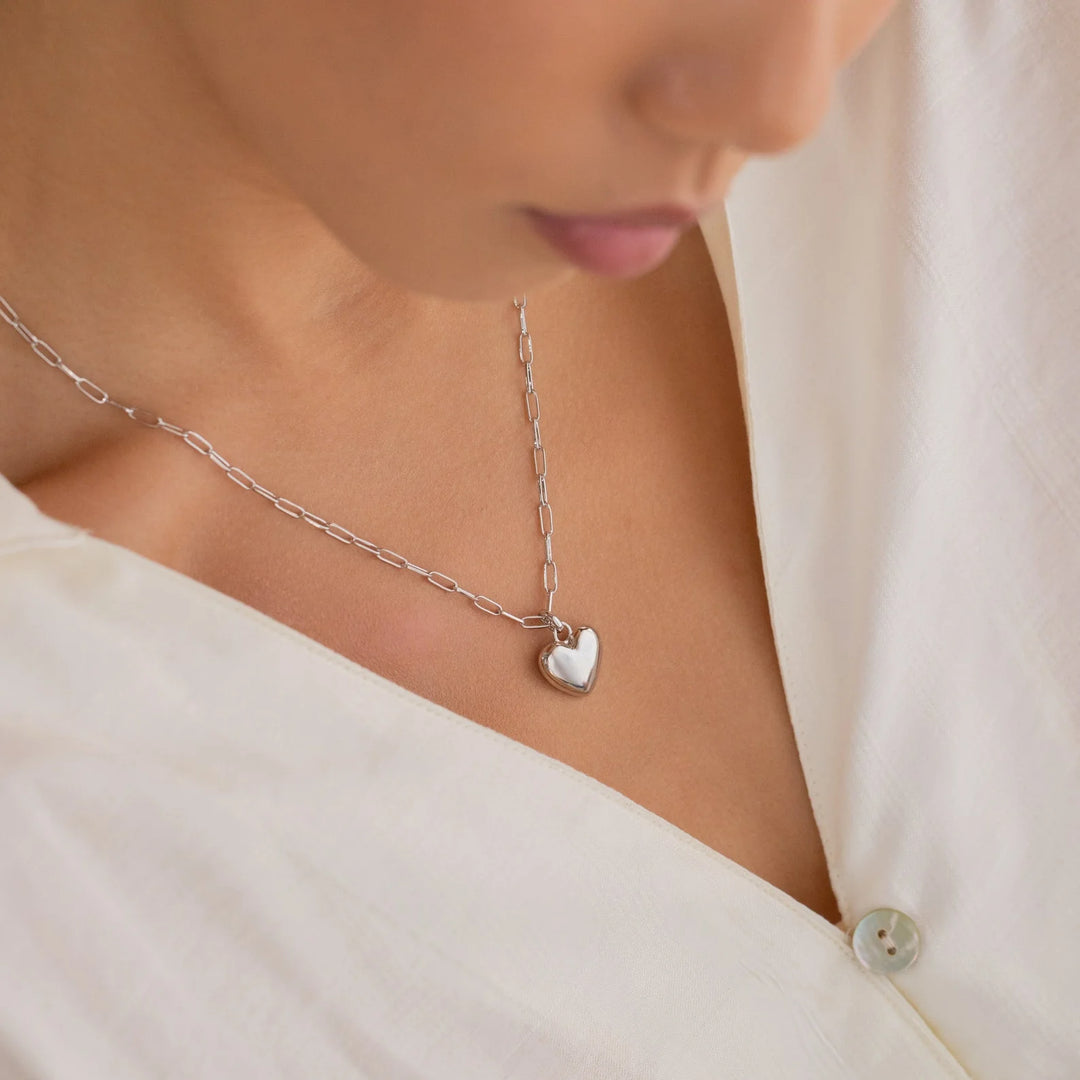 Necklace with a heart-shaped pendant worn by a person in a white outfit.