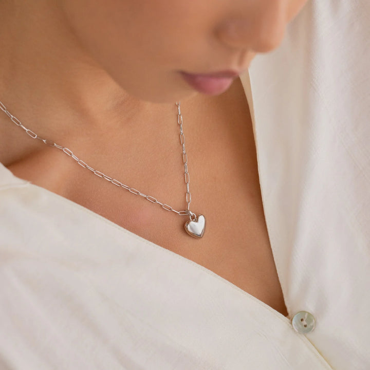 Necklace with a heart-shaped pendant worn by a person in a white outfit.