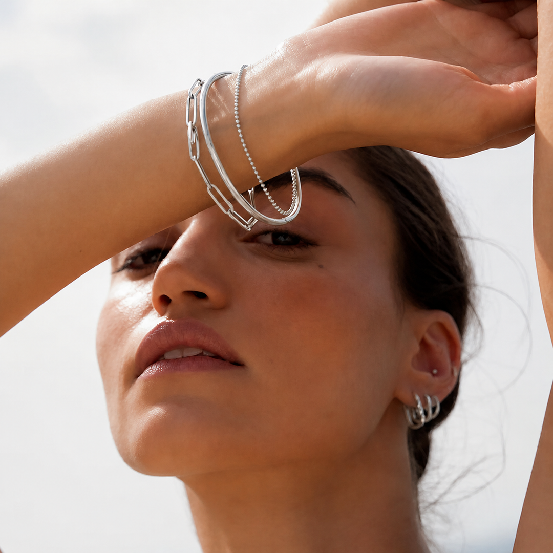 Close-up of a woman's face with silver jewelry on her arm and hand.