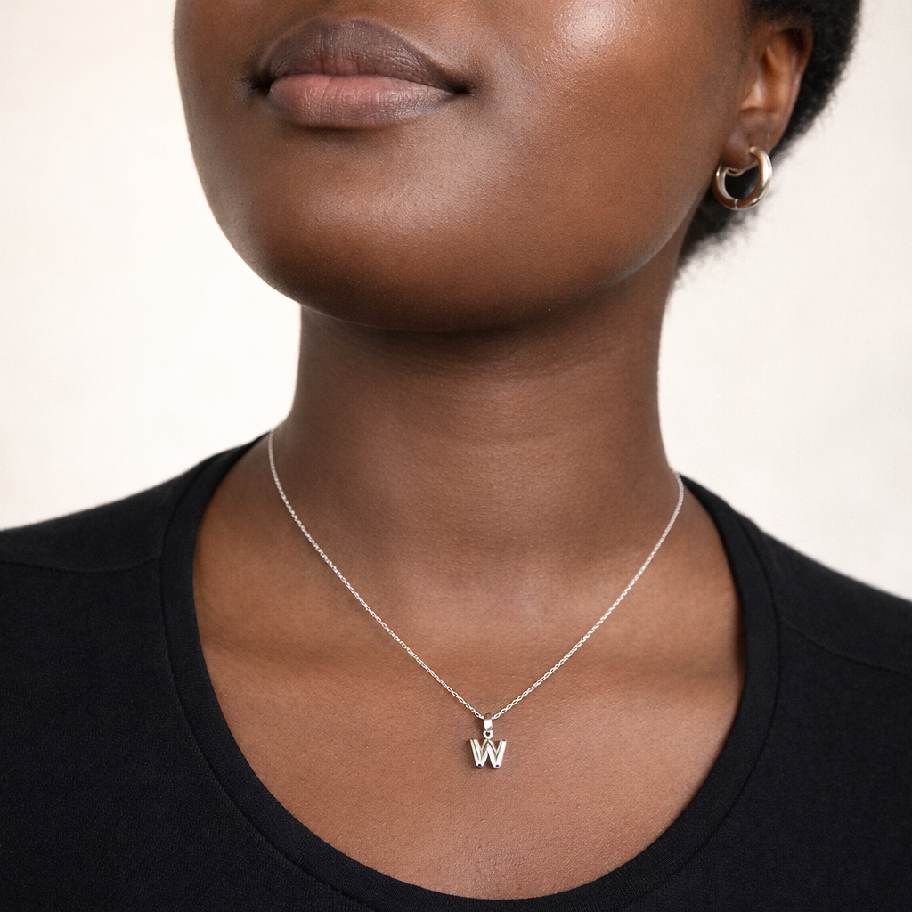 Person wearing a silver necklace with a 'W' pendant on a neutral background