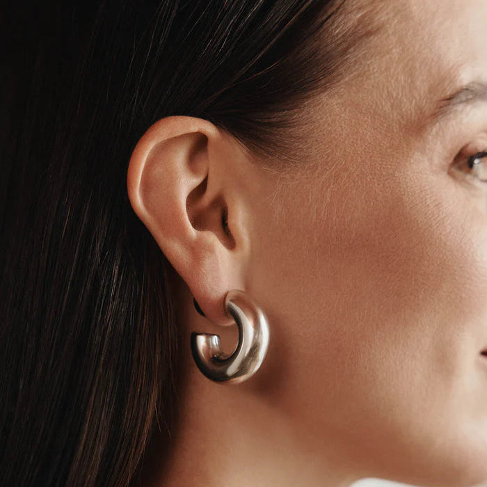 Close-up of a person wearing a silver hoop earring with a neutral background