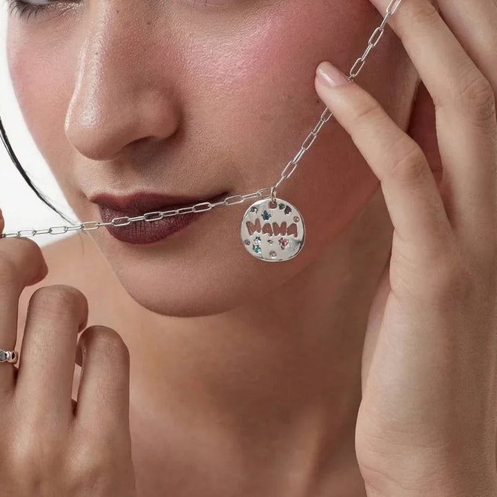 Close-up of a person wearing a silver necklace with a 'MAMA' pendant.