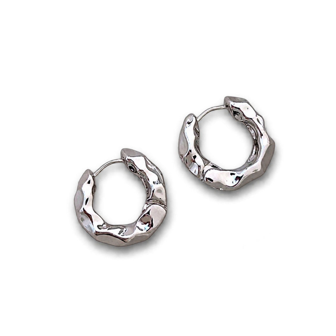 A pair of textured silver huggie hoop earrings with a polished, hammered finish, displayed on a clean white background.