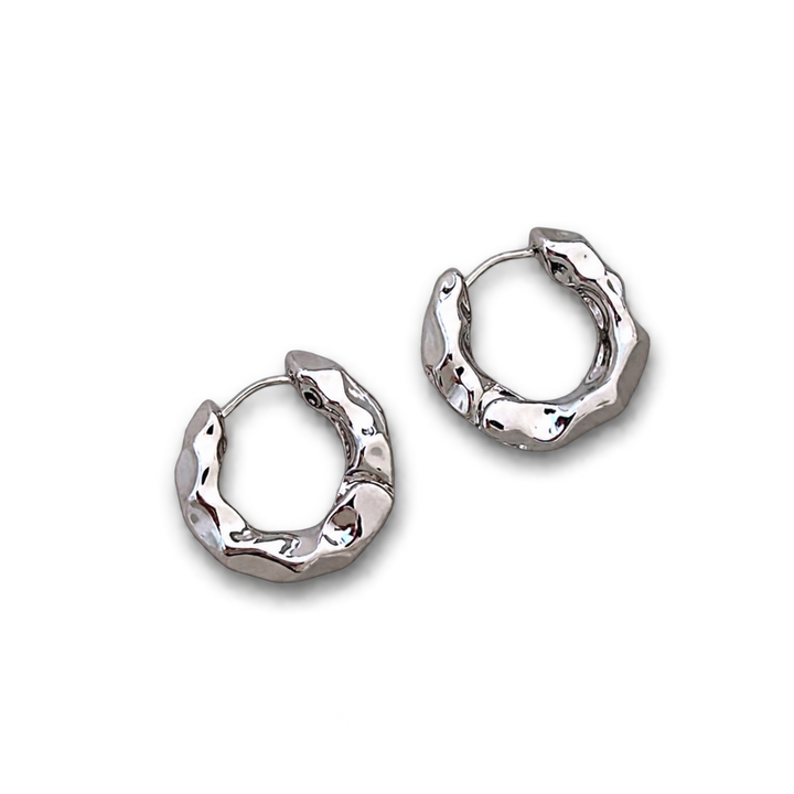 A pair of textured silver huggie hoop earrings with a polished, hammered finish, displayed on a clean white background.