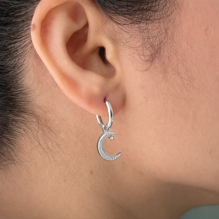 Silver hoop earring with a moon charm worn by a person
