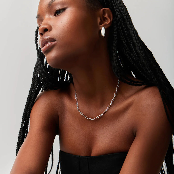Woman wearing a black strapless top and silver necklace against a neutral background