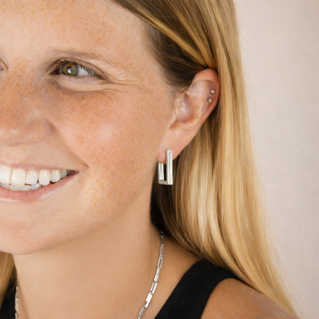 Close-up of a woman wearing silver hoop earrings with a plain background