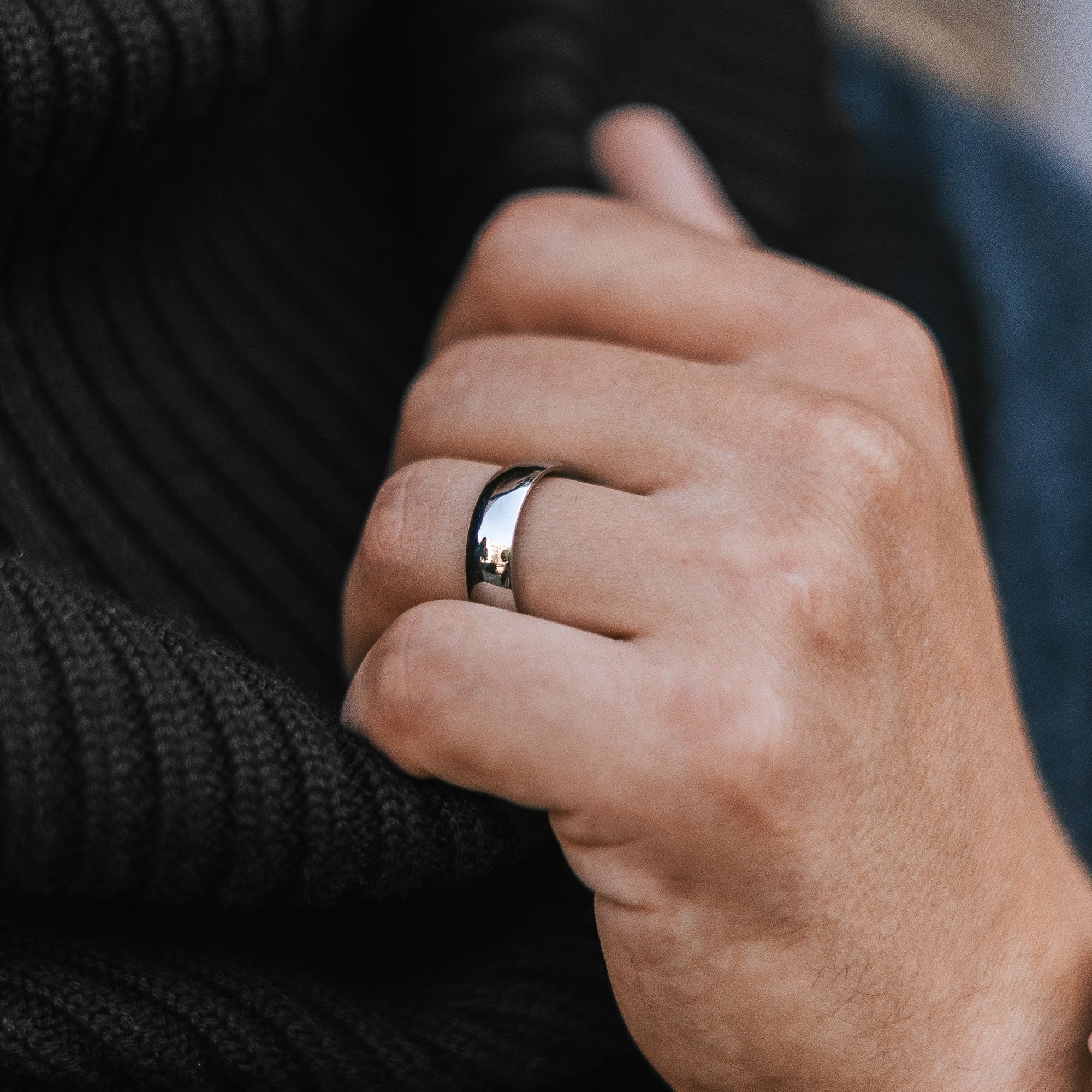 Hand wearing a silver ring with a blurred background