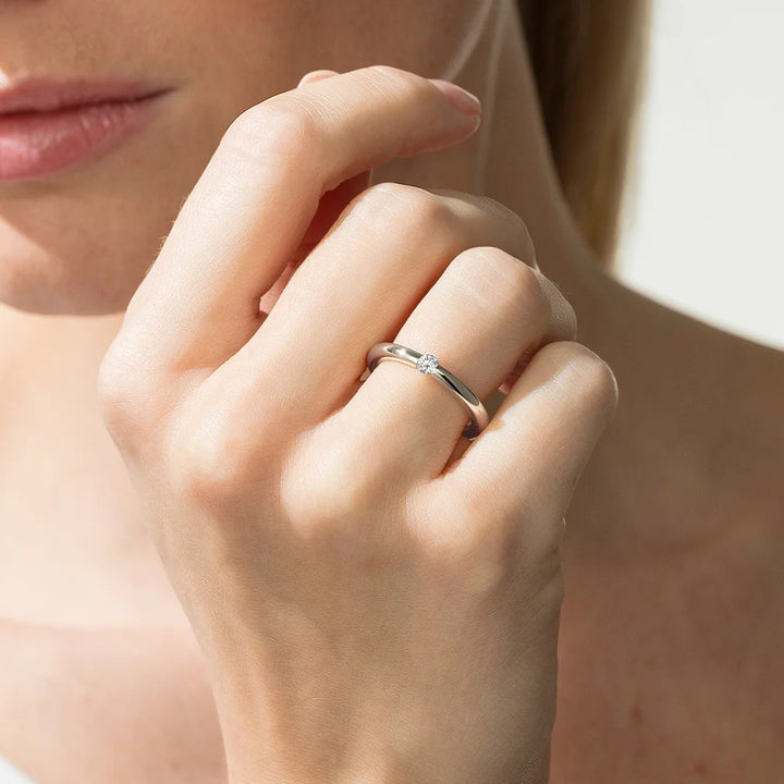 Close-up of a hand wearing a silver ring with a diamond on a blurred background