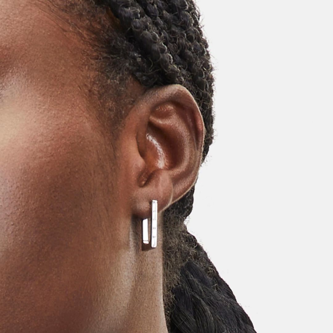 Close-up of an ear wearing a silver hoop earring on a plain background