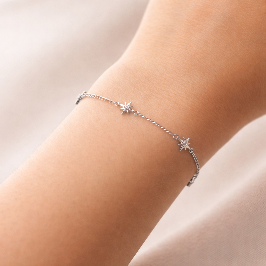 Silver bracelet with star charms on a person's wrist against a neutral background