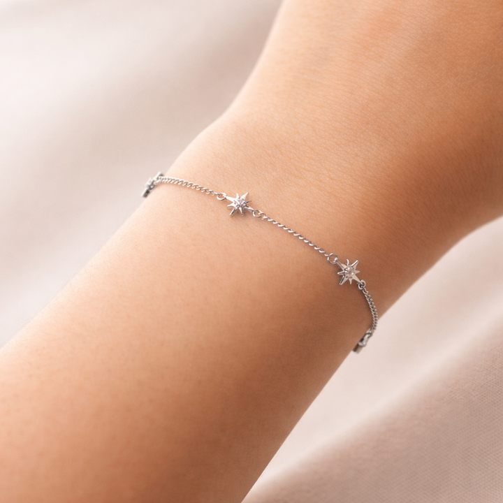 Silver bracelet with star charms on a person's wrist against a neutral background