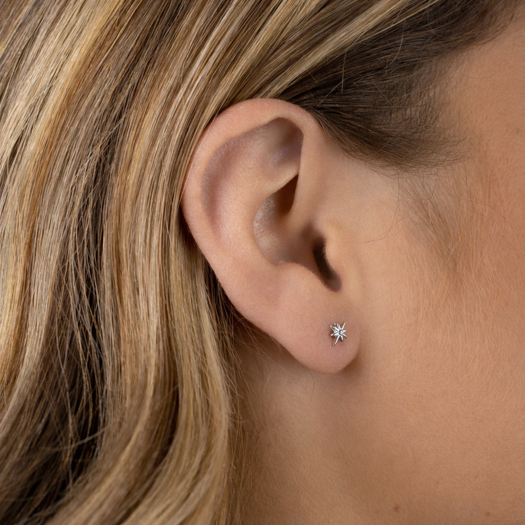 Close-up of an ear wearing a small diamond stud earring with blonde hair.