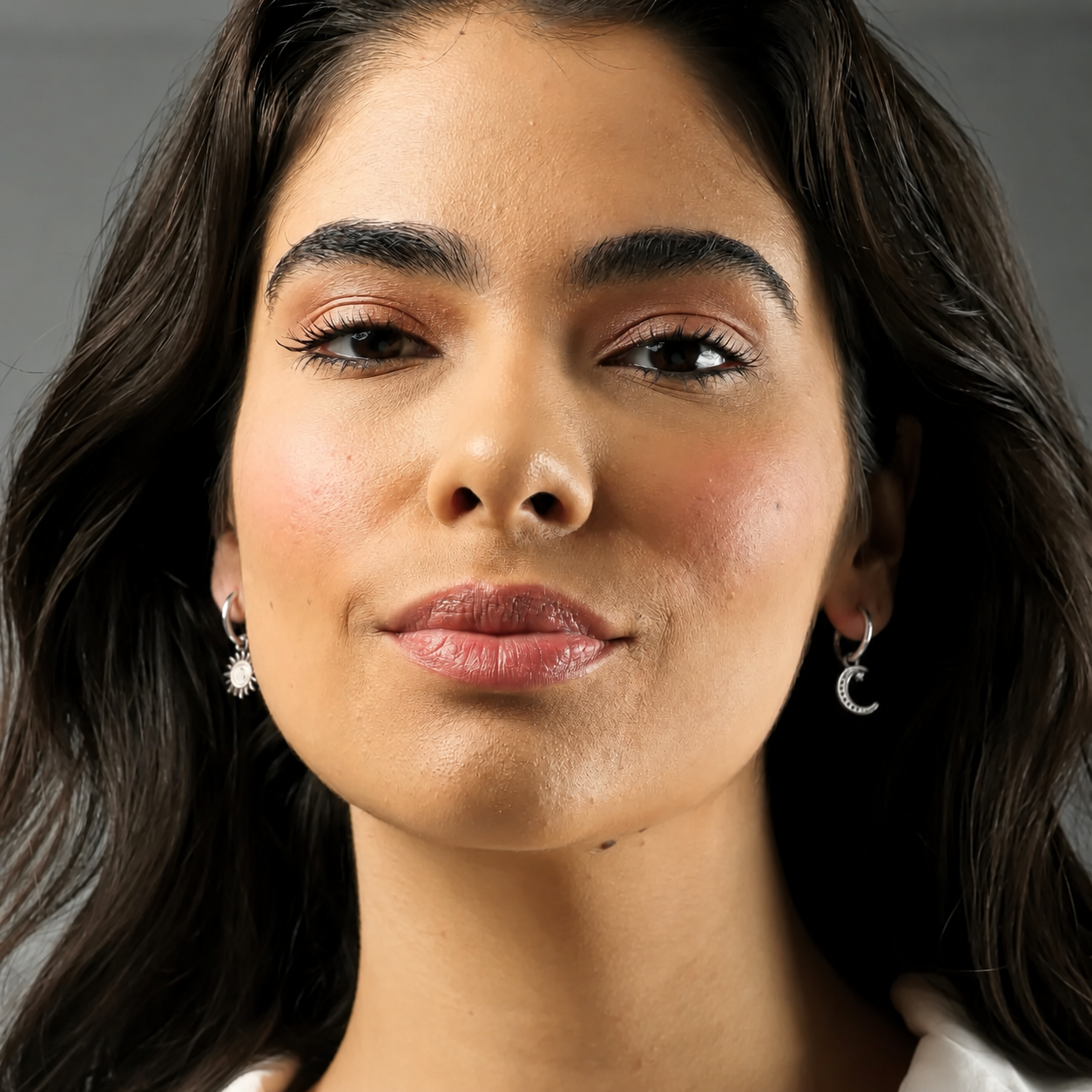 Close-up of a woman with dark hair and earrings against a neutral background