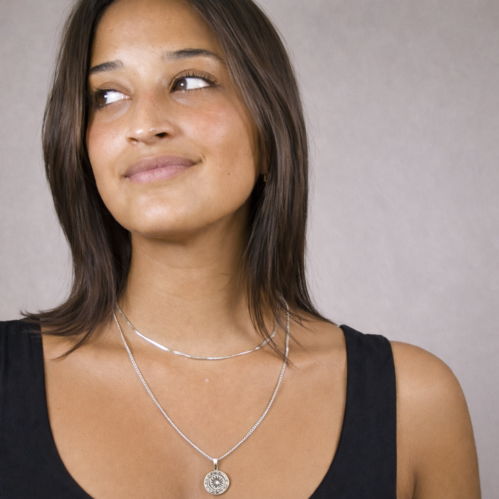 Woman wearing a silver necklace with a pendant against a neutral background