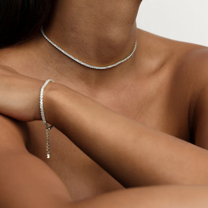 Silver necklace and bracelet on a person's neck and wrist against a neutral background