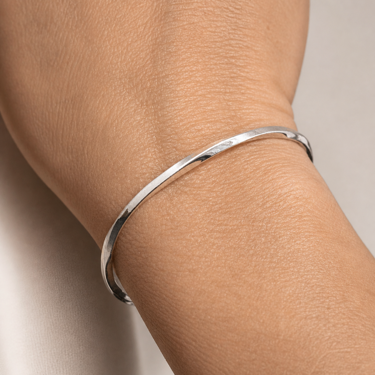 Silver bracelet on a person's wrist against a neutral background