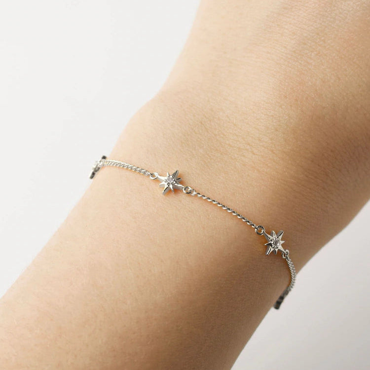 Silver star bracelet on a person's wrist against a light background