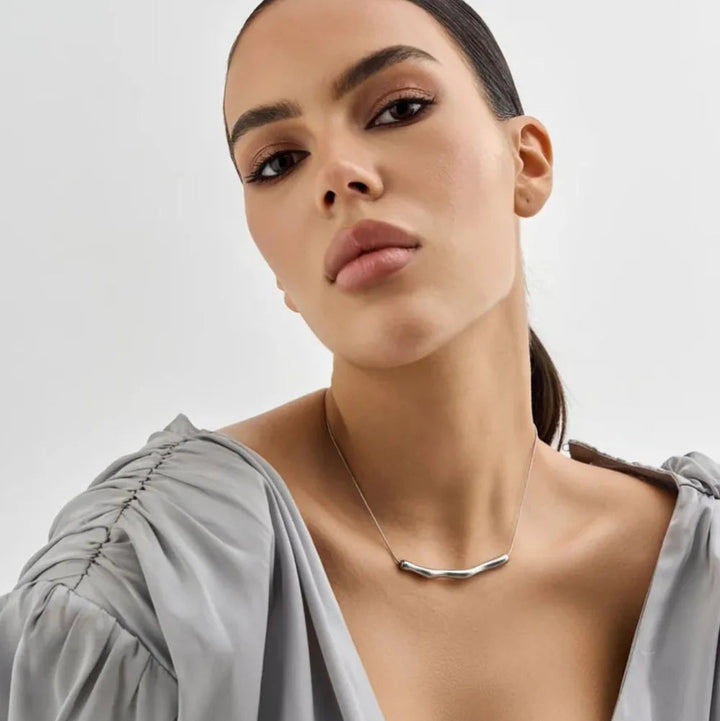 Woman wearing a silver necklace against a plain background