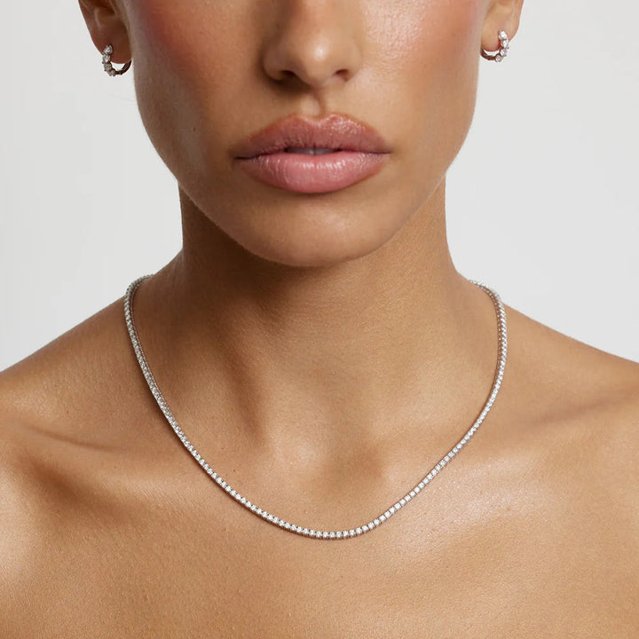 Close-up of a person wearing a silver necklace on a plain background