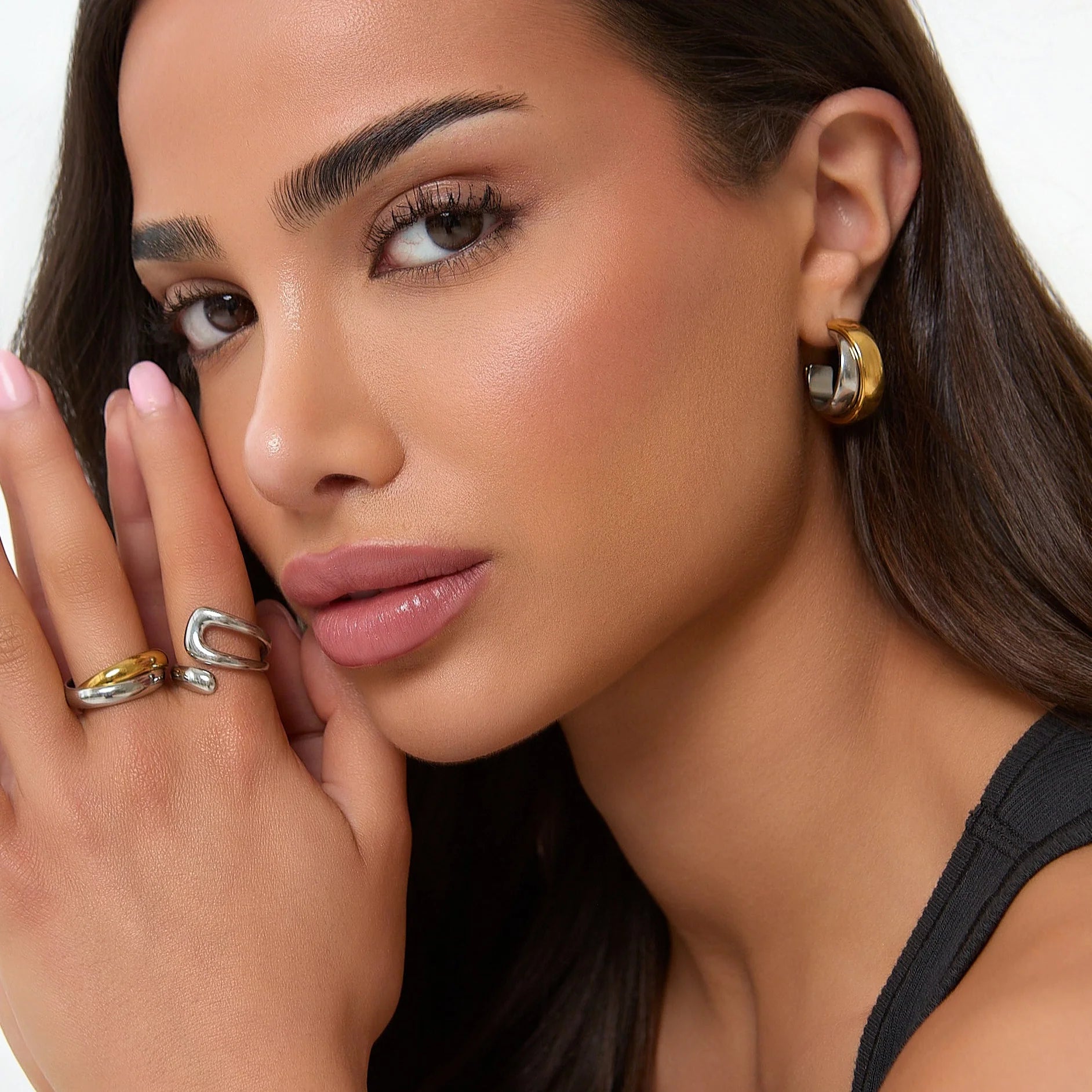 Close-up of a woman's face with jewelry, including earrings and rings.