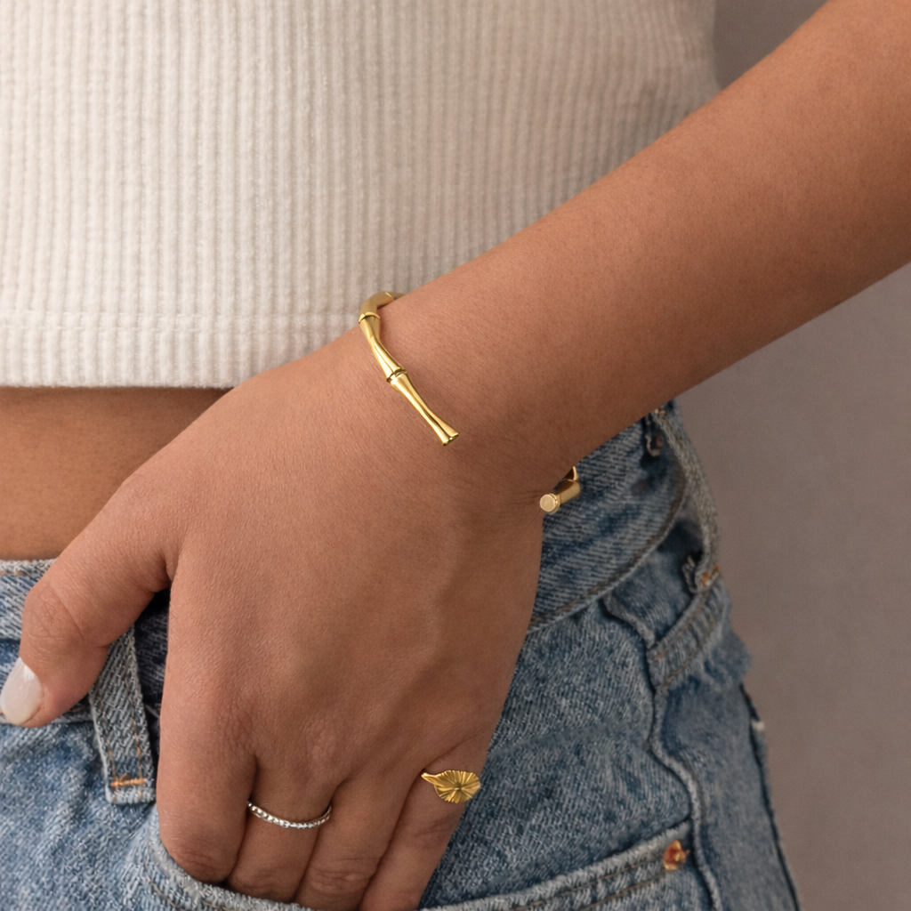 Gold bracelet and ring on a wrist with a neutral background