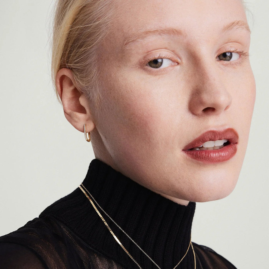 Woman wearing a black turtleneck and gold jewelry against a plain background