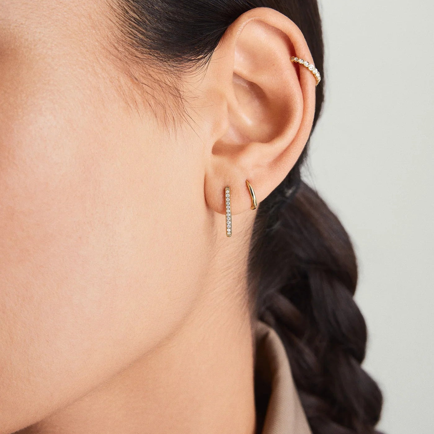 Close-up of a person's ear wearing gold hoop earrings with a neutral background