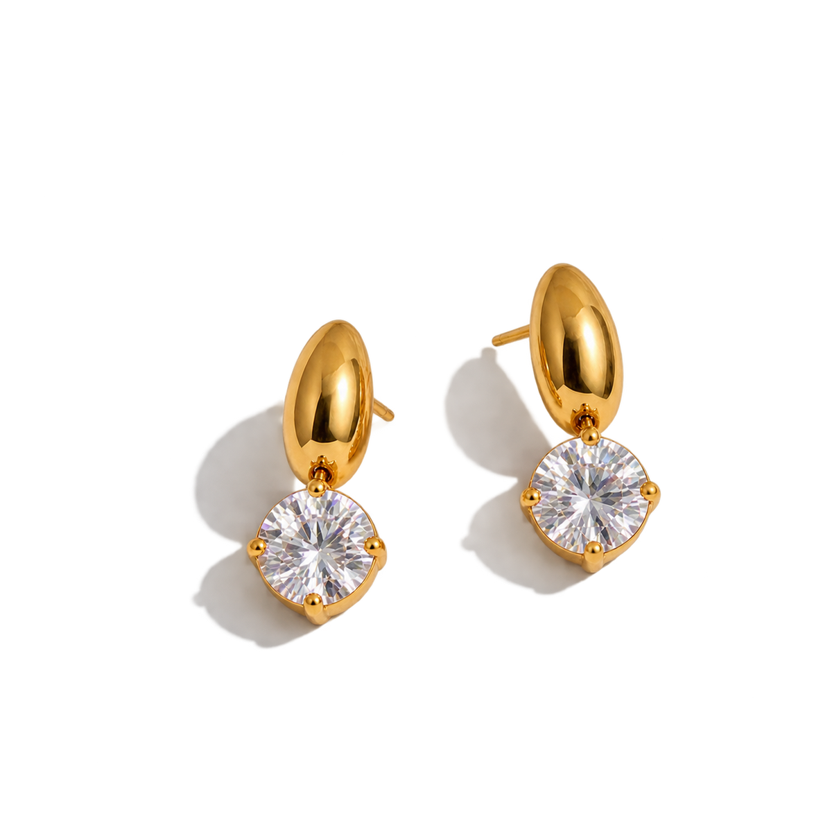 A pair of gold drop earrings with a large round clear gemstone in a prong setting, shown on a clean white background with soft shadows.