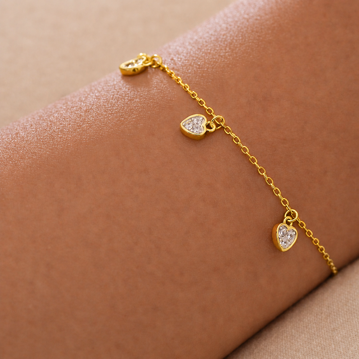 Gold bracelet with heart-shaped charms on a wrist against a beige background