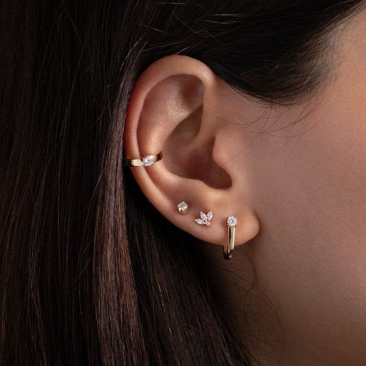 Close-up of an ear wearing gold and diamond earrings with dark hair.