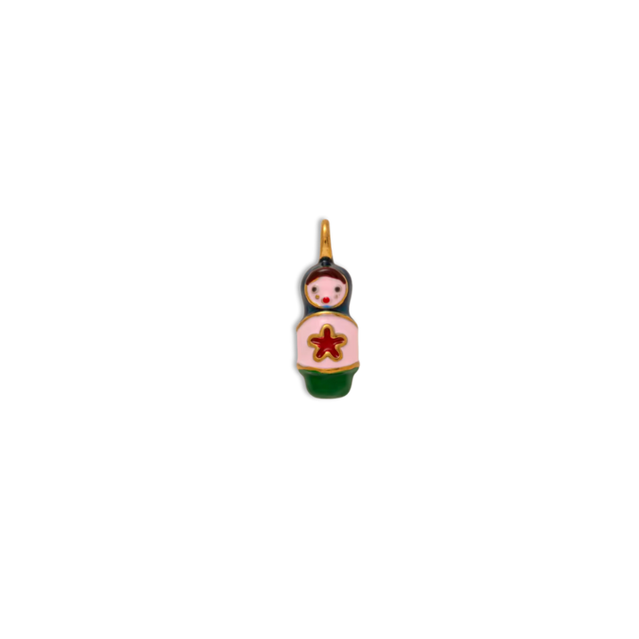 A small enamel charm shaped like a nesting doll, featuring a light pink body, dark green base, black hair, and a red star on the chest, with a gold-tone loop at the top.