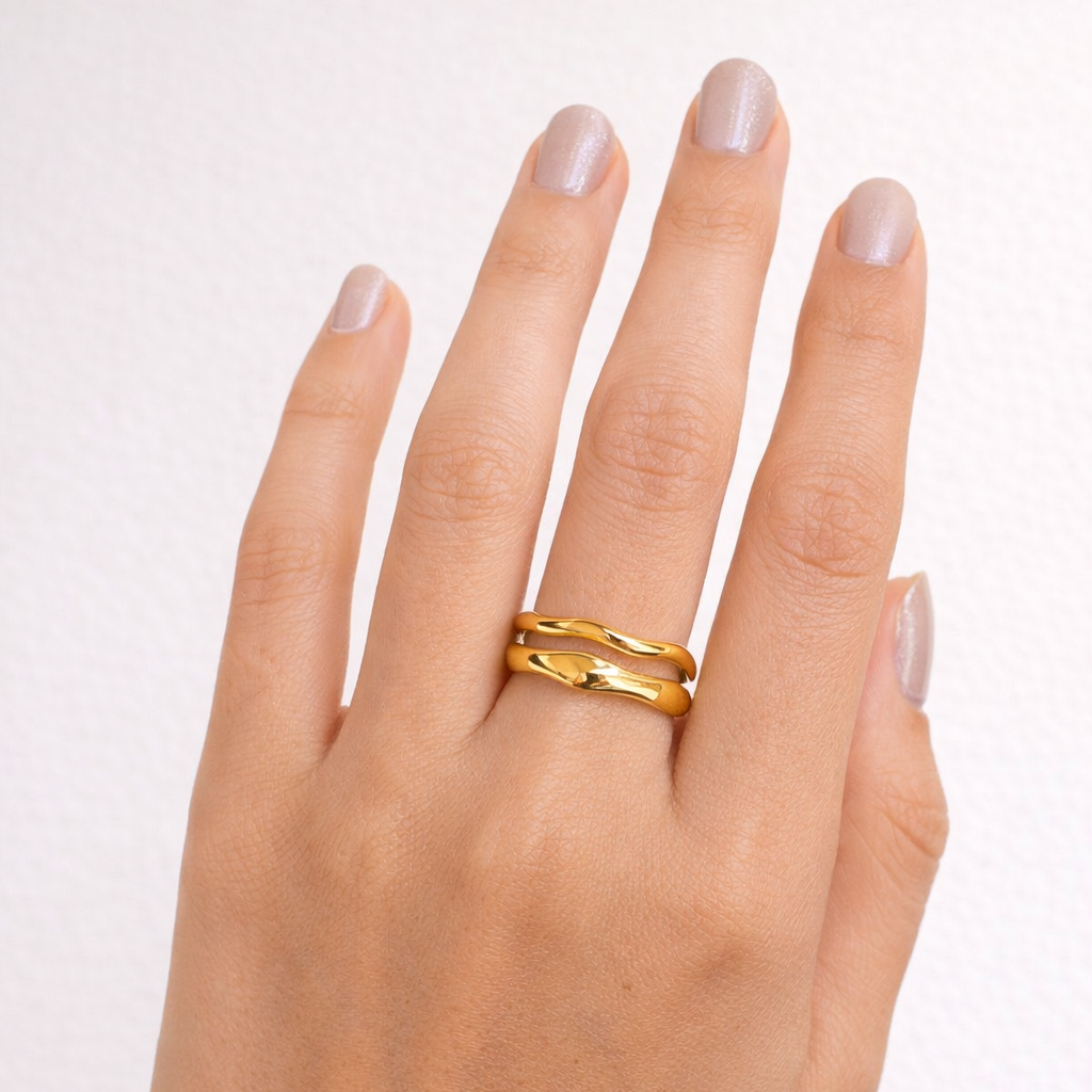 Hand wearing a gold ring on a plain background