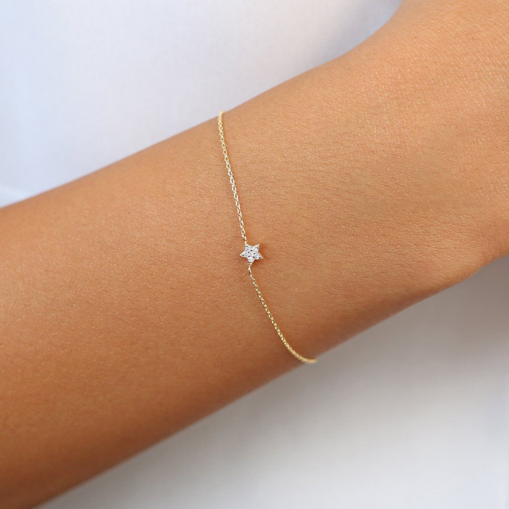 Gold bracelet with a star-shaped charm on a wrist against a white background