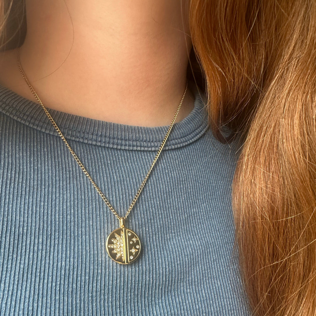 Person wearing a gold necklace with a circular pendant on a blue shirt