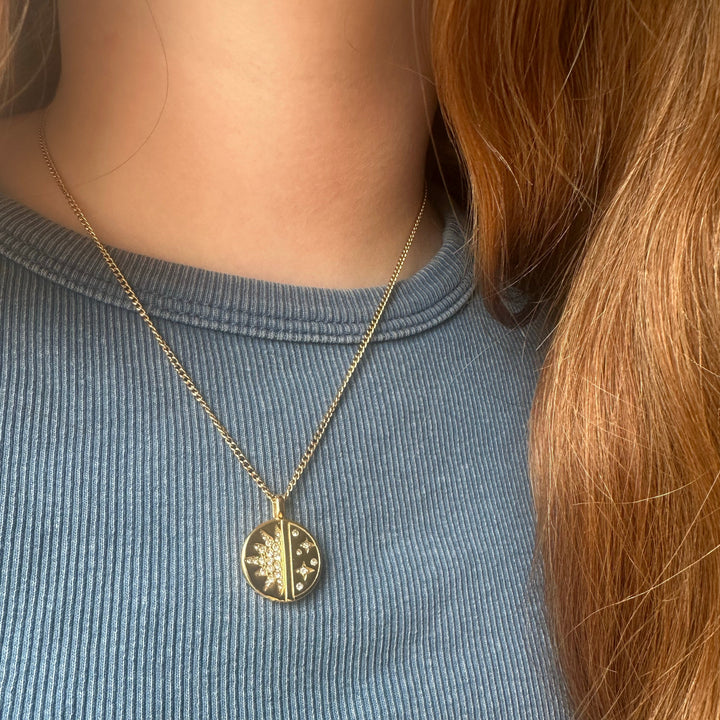 Person wearing a gold necklace with a circular pendant on a blue shirt