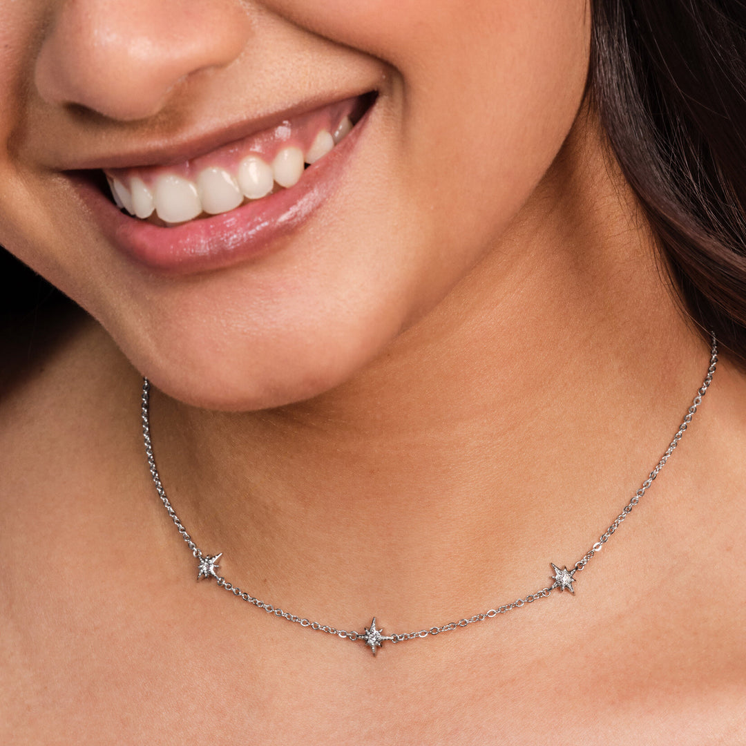 Close-up of a woman wearing a delicate silver necklace with star-shaped pendants.