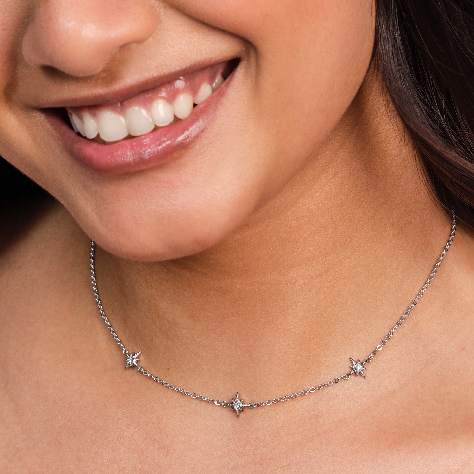 Close-up of a woman wearing a delicate silver necklace with star-shaped pendants.